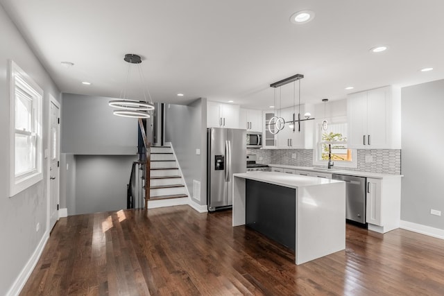 kitchen featuring backsplash, stainless steel appliances, pendant lighting, white cabinets, and a center island