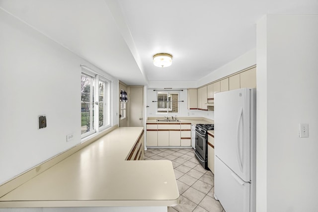 kitchen featuring sink, gas range, cream cabinetry, white fridge, and kitchen peninsula