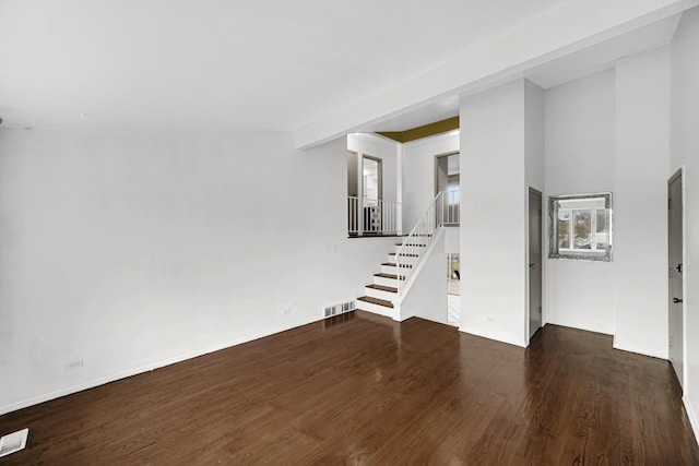 unfurnished living room featuring beam ceiling and dark wood-type flooring