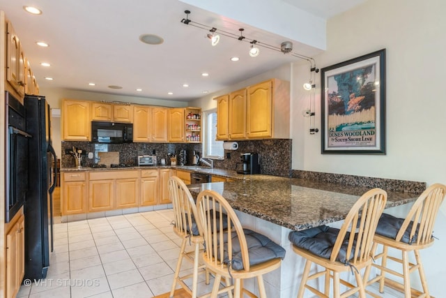 kitchen with kitchen peninsula, dark stone counters, black appliances, light tile patterned floors, and a breakfast bar area