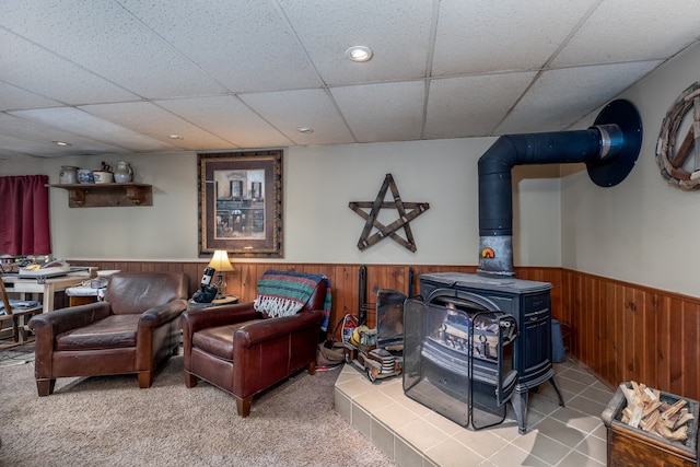 living room with a wainscoted wall, a paneled ceiling, wooden walls, and a wood stove