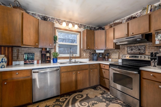 kitchen featuring under cabinet range hood, decorative backsplash, appliances with stainless steel finishes, and a sink