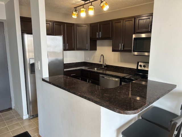 kitchen with sink, decorative light fixtures, kitchen peninsula, dark stone counters, and appliances with stainless steel finishes