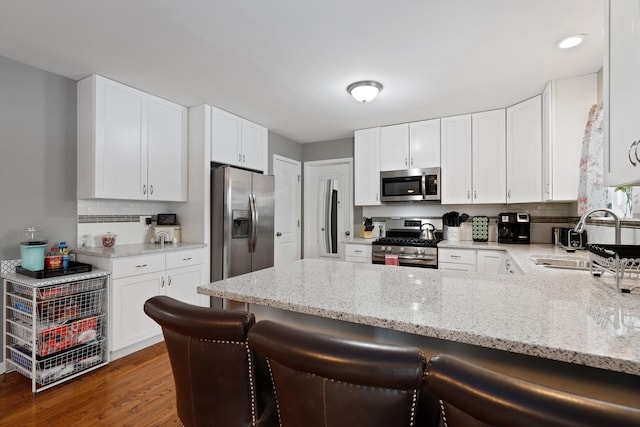 kitchen featuring a breakfast bar, kitchen peninsula, sink, stainless steel appliances, and white cabinets