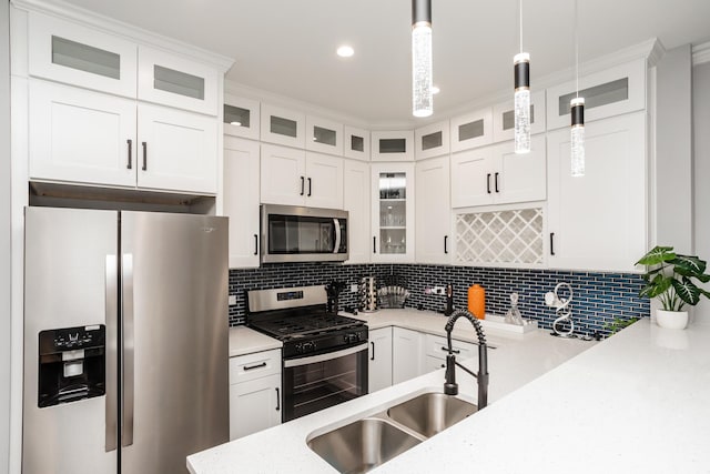 kitchen with decorative backsplash, appliances with stainless steel finishes, sink, white cabinetry, and hanging light fixtures