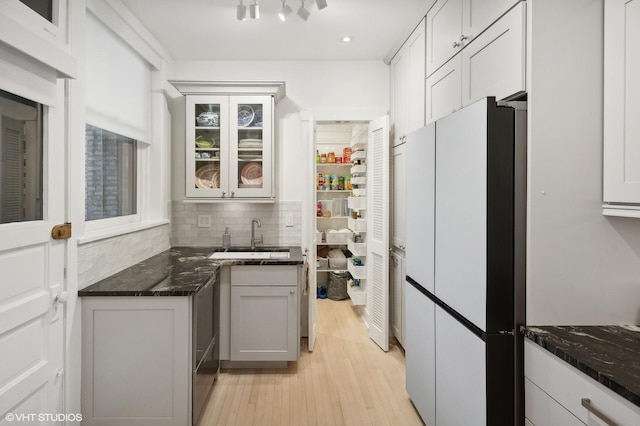 kitchen featuring dark stone counters, white refrigerator, sink, light wood-type flooring, and white cabinetry