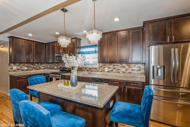 kitchen featuring pendant lighting, a breakfast bar, light stone countertops, appliances with stainless steel finishes, and a kitchen island