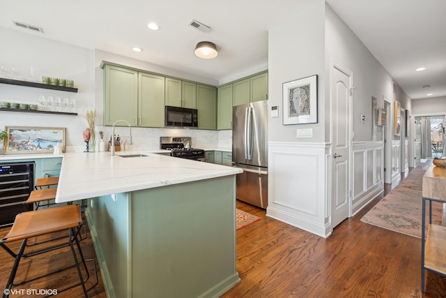 kitchen with kitchen peninsula, wine cooler, appliances with stainless steel finishes, sink, and green cabinetry