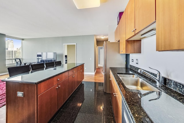 kitchen featuring stainless steel fridge, a breakfast bar, sink, dark stone countertops, and a kitchen island