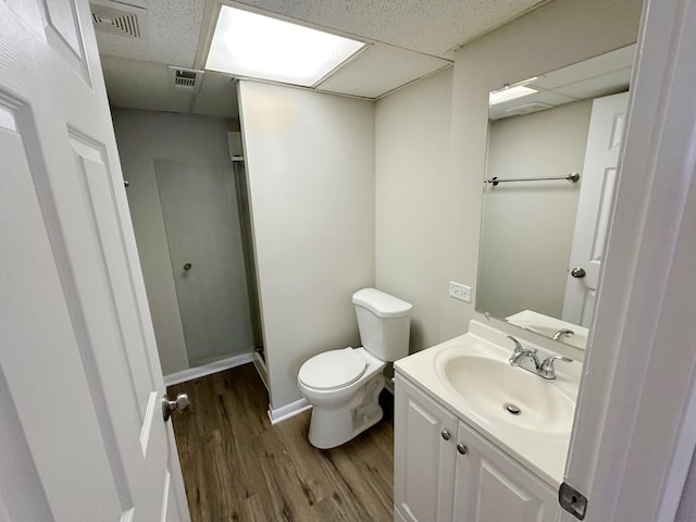 bathroom with hardwood / wood-style floors, a drop ceiling, toilet, and vanity