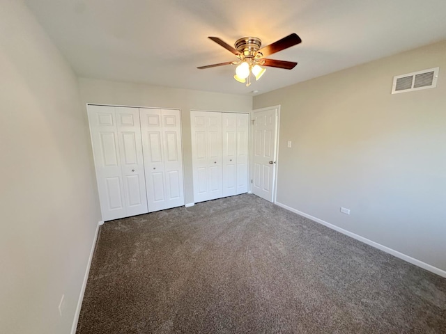 unfurnished bedroom with dark carpet, ceiling fan, and multiple closets