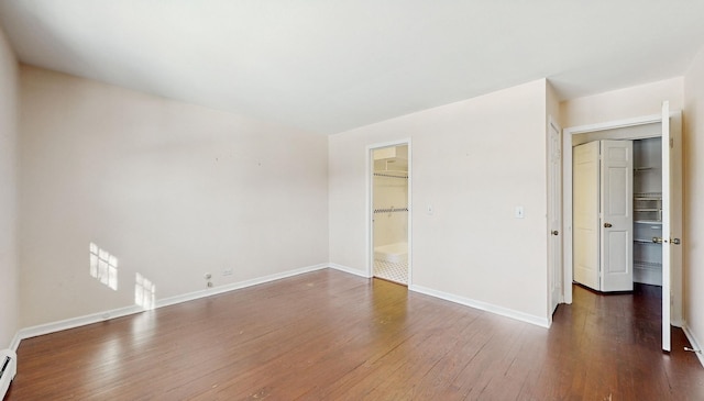 unfurnished room featuring a baseboard heating unit and dark hardwood / wood-style floors