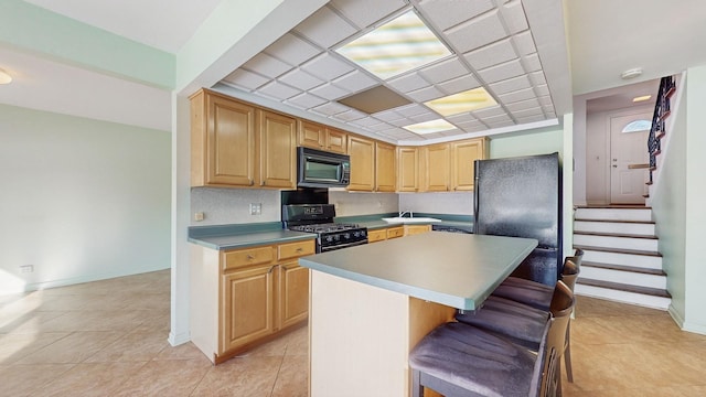 kitchen with black appliances, a breakfast bar, a kitchen island, light brown cabinets, and sink