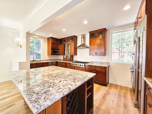 kitchen with light stone counters, wall chimney range hood, a center island, and stainless steel appliances