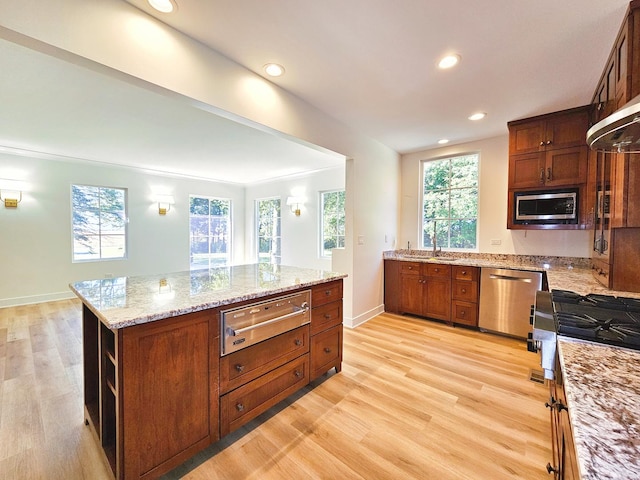 kitchen with light stone counters, stainless steel appliances, a kitchen island, and light wood-type flooring