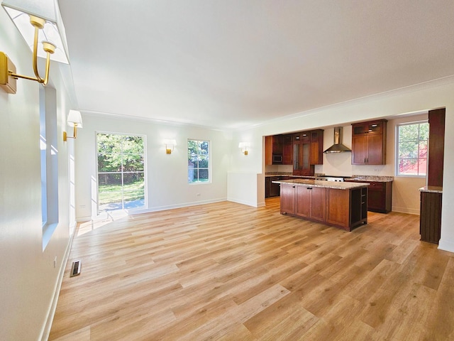 kitchen with a kitchen island, a healthy amount of sunlight, light hardwood / wood-style floors, and wall chimney range hood