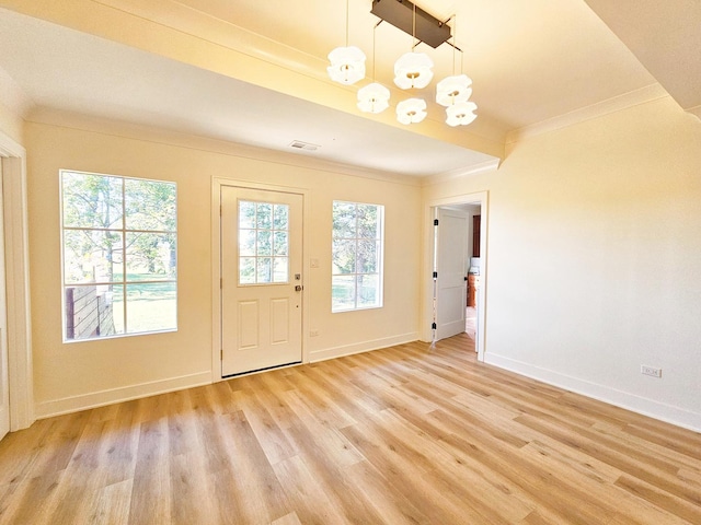 foyer entrance with light wood-type flooring, a notable chandelier, a wealth of natural light, and ornamental molding