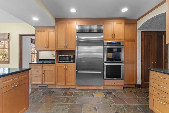 kitchen with ornamental molding, dark stone countertops, and appliances with stainless steel finishes