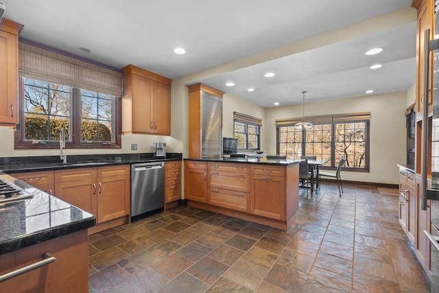 kitchen featuring kitchen peninsula, pendant lighting, sink, dark stone counters, and stainless steel appliances