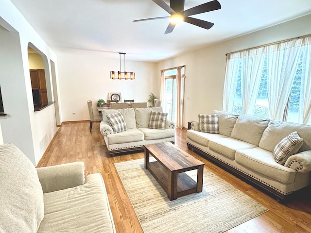 living room with ceiling fan with notable chandelier and light hardwood / wood-style floors