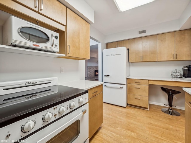 kitchen with white appliances, light hardwood / wood-style floors, and a brick fireplace