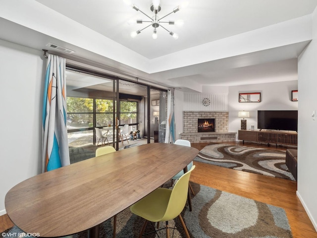 dining room featuring hardwood / wood-style flooring, an inviting chandelier, and a brick fireplace