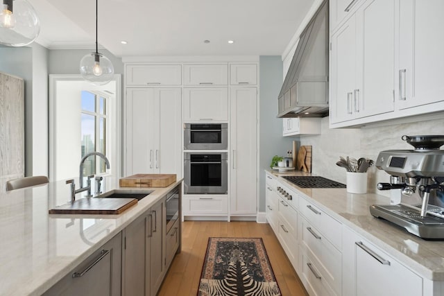 kitchen with pendant lighting, sink, light stone countertops, custom range hood, and white cabinetry