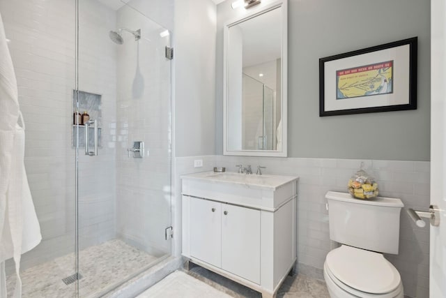 bathroom featuring tile patterned floors, toilet, a shower with door, vanity, and tile walls