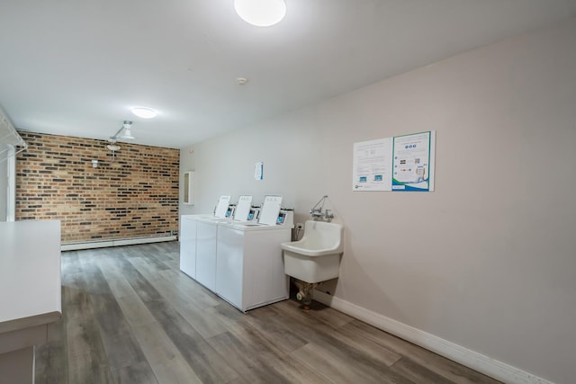 clothes washing area with sink, light hardwood / wood-style floors, washer and clothes dryer, and brick wall