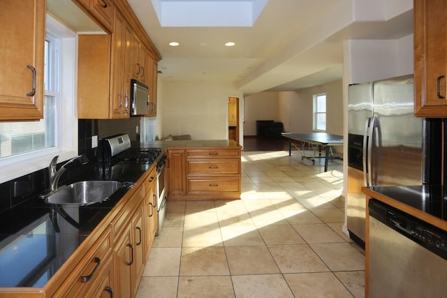 kitchen with sink, a skylight, light tile patterned floors, tile counters, and stainless steel appliances