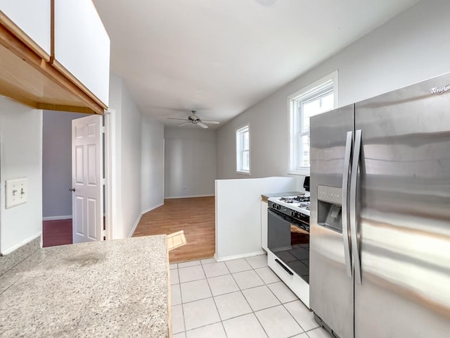 kitchen featuring white cabinetry, ceiling fan, stainless steel fridge, light tile patterned floors, and white gas range oven