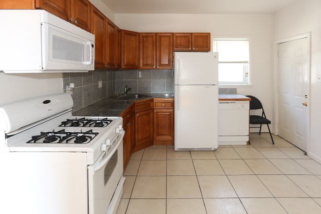 kitchen with decorative backsplash, white appliances, light tile patterned flooring, and sink