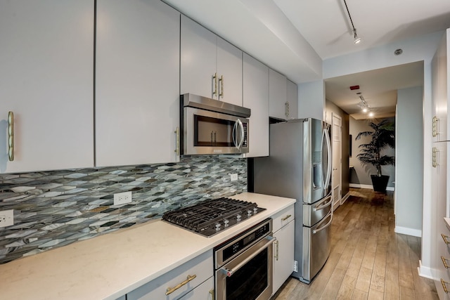 kitchen featuring rail lighting, light wood-type flooring, backsplash, and appliances with stainless steel finishes