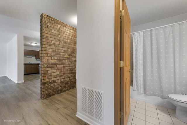 bathroom featuring wood-type flooring, shower / bath combination with curtain, brick wall, and toilet