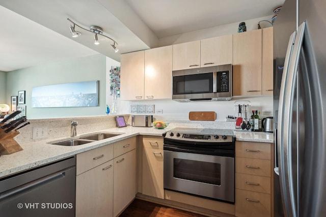 kitchen featuring appliances with stainless steel finishes, light stone counters, a sink, and light brown cabinetry