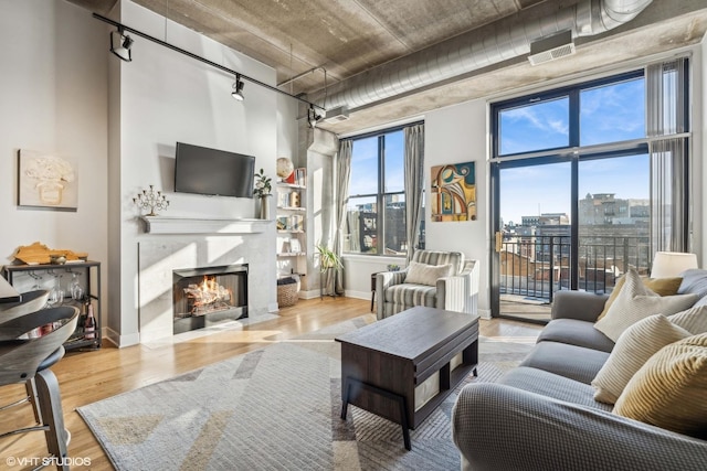 living area with a fireplace with flush hearth, plenty of natural light, a towering ceiling, and wood finished floors