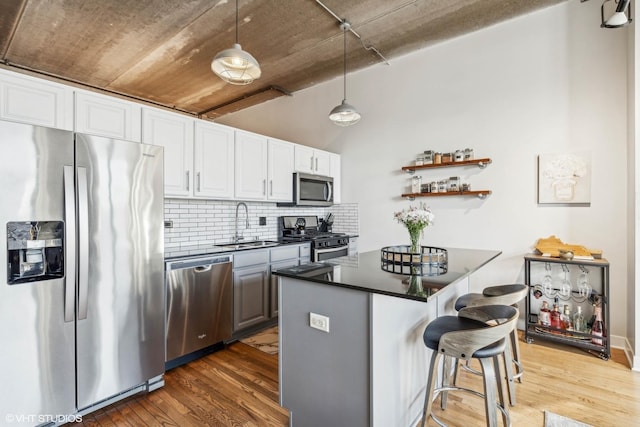 kitchen featuring a breakfast bar area, wood finished floors, a sink, appliances with stainless steel finishes, and dark countertops