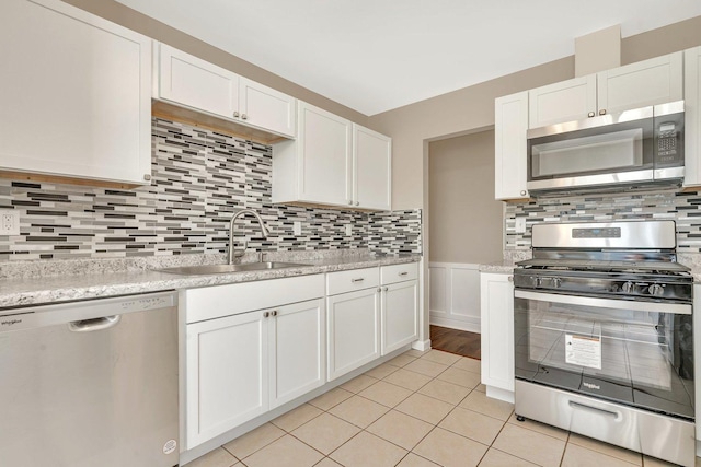 kitchen with stainless steel appliances, sink, white cabinets, light tile patterned floors, and decorative backsplash