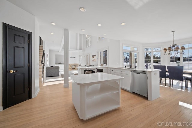 kitchen featuring kitchen peninsula, pendant lighting, sink, white cabinetry, and stainless steel dishwasher