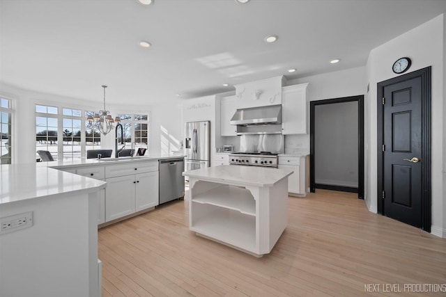 kitchen featuring stainless steel appliances, white cabinetry, hanging light fixtures, a kitchen island, and wall chimney range hood