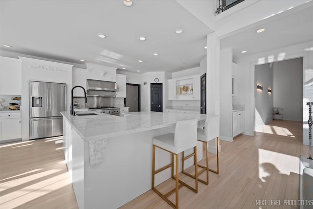 kitchen featuring light stone counters, stainless steel appliances, white cabinets, ventilation hood, and sink