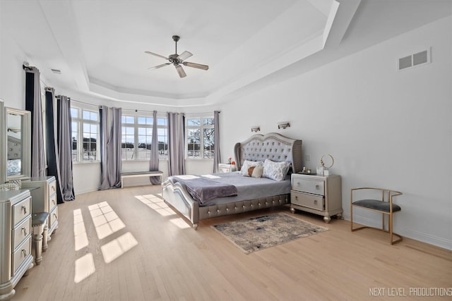 bedroom featuring light wood-type flooring, ceiling fan, and a tray ceiling