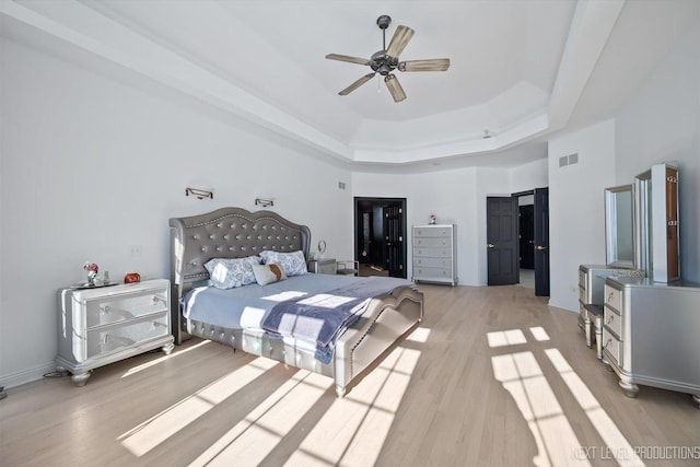 bedroom with ceiling fan, light hardwood / wood-style flooring, and a tray ceiling