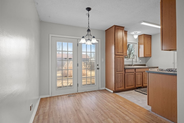 kitchen with pendant lighting, sink, light wood-type flooring, a textured ceiling, and a notable chandelier