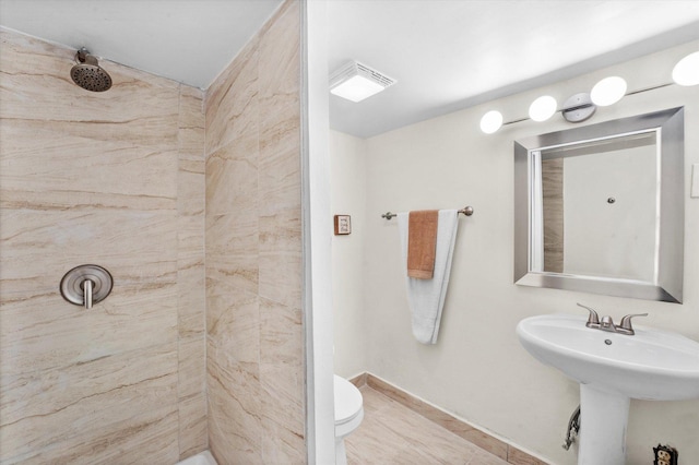 bathroom with a tile shower, sink, and toilet