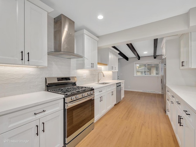 kitchen with beam ceiling, stainless steel appliances, white cabinetry, and wall chimney range hood