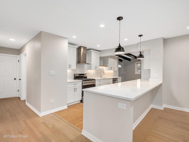 kitchen featuring wall chimney exhaust hood, stainless steel appliances, pendant lighting, light hardwood / wood-style floors, and white cabinetry