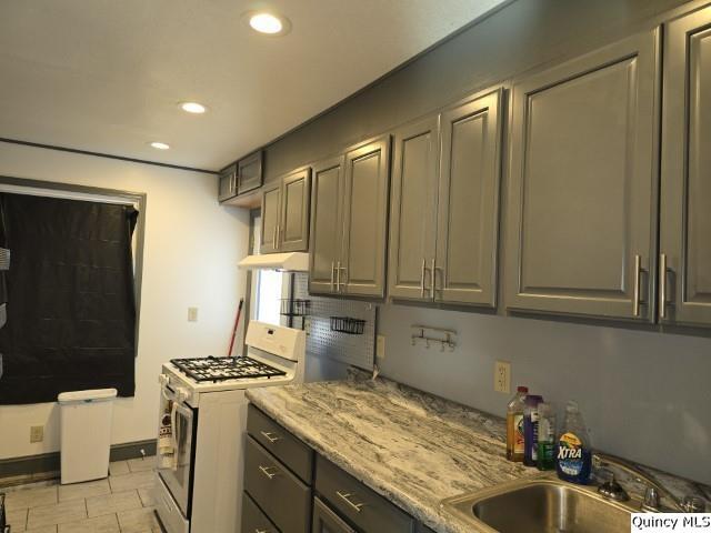 kitchen featuring sink, light tile patterned floors, light stone counters, and gas range gas stove