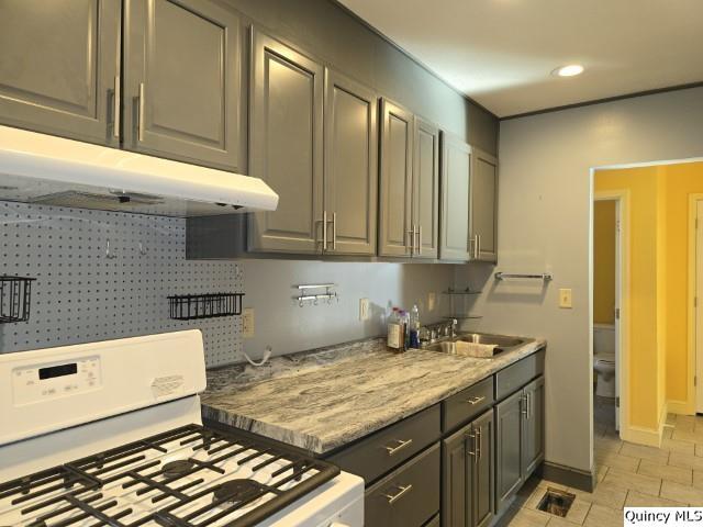 kitchen with sink, light stone counters, and white gas range oven