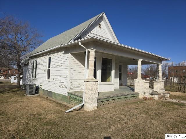 view of property exterior featuring covered porch, central AC, and a lawn